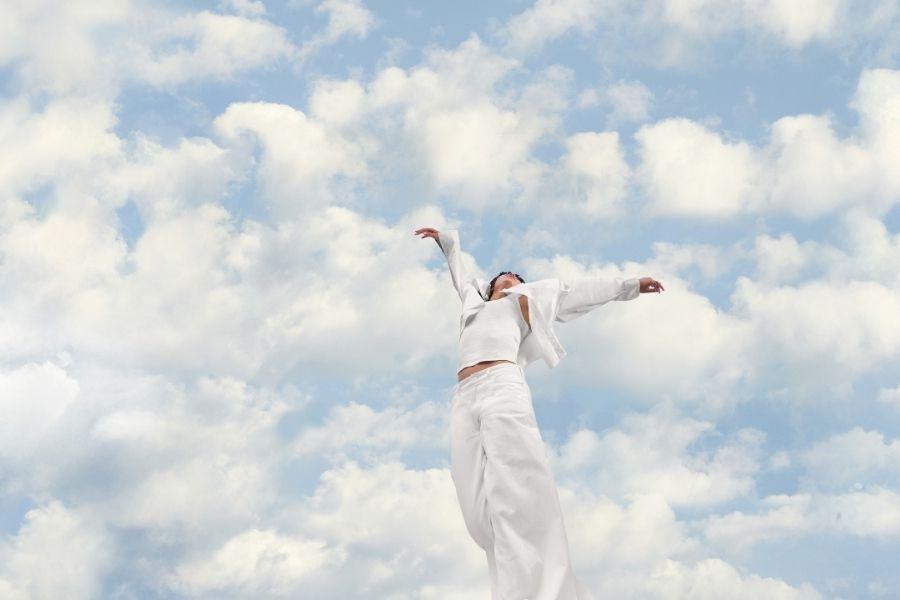Já é conhecida a cor do ano para 2026. Na imagem vemos uma mulher de braços abertos, vestida de branco, com um fundo de céu com nuvens.